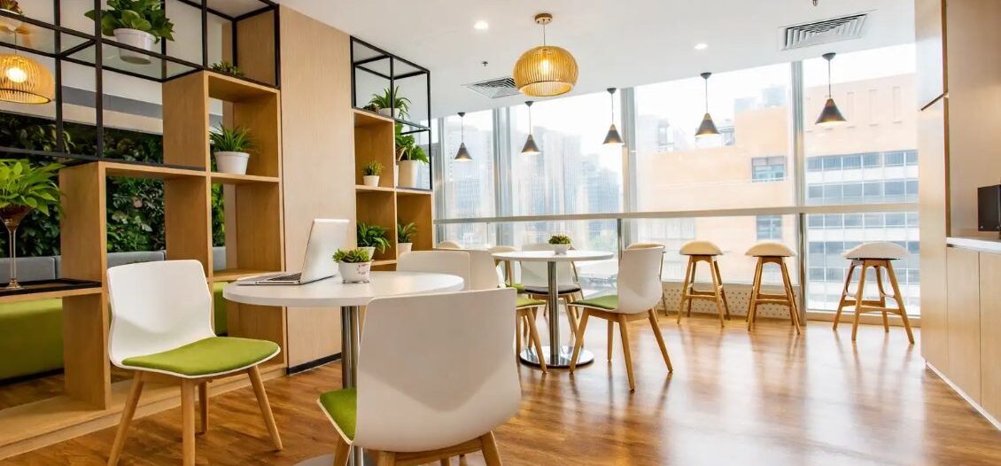 Agencement d’un espace collaboratif avec mobilier collectif sur mesure, tables rondes, étagères bois végétalisées et espace coworking lumineux.