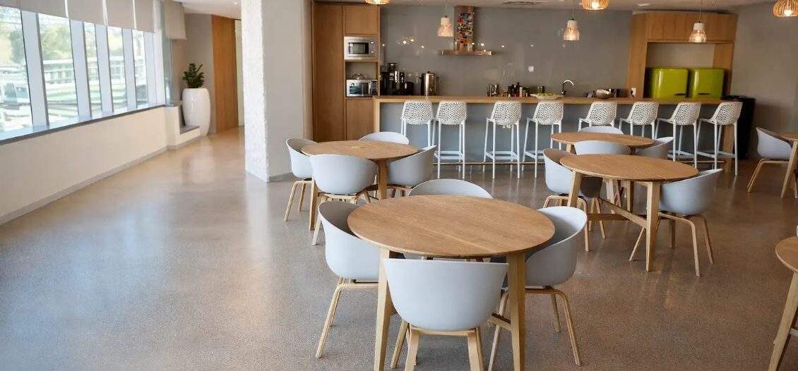 Agencement d’un espace commun de résidence étudiante avec tables bois, chaises design et cuisine ouverte avec comptoir bar réalisé sur mesure.